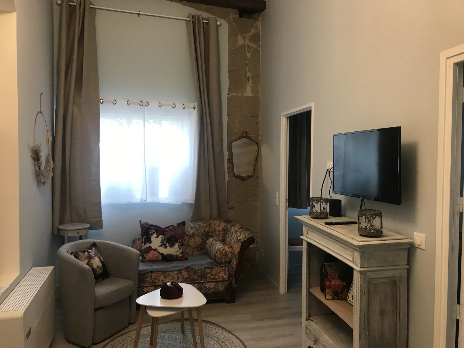 Le salon de L’Apothicaire, avec son canapé fleuri, sa cheminée et son mur en pierre.